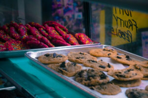 tray of chocolate chip cookies in the foreground and red fruity pebble cookies in the back