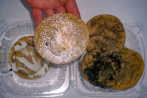 hand holding a cookie with three cookies in a container behind